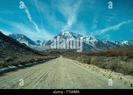 Dirt road leading towards mountains against sky Stock Photo