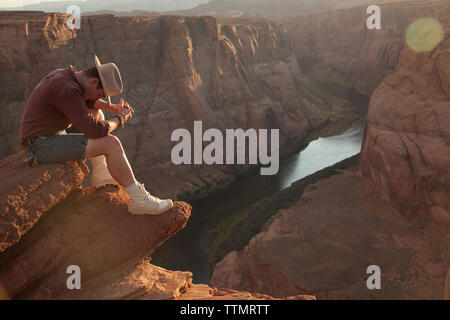 Full length of young man sitting on rock by Horseshoe Bend at desert Stock Photo
