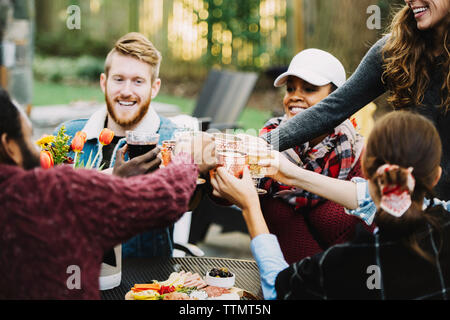 Happy friends toasting drinks while sitting in backyard Stock Photo