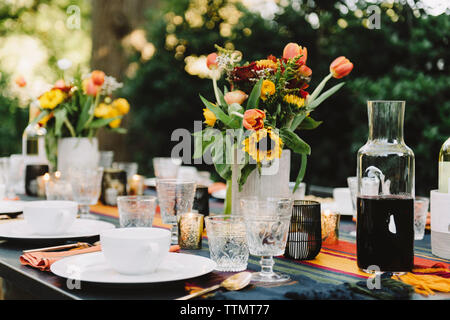 Flower vases with drinks and crockery arranged on table in backyard Stock Photo