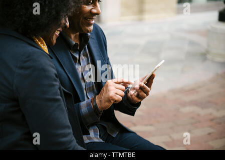 Happy woman looking at man using mobile phone in city Stock Photo
