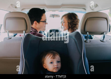 Mom and dad driving in white car with baby in a car seat in the back Stock Photo