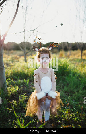 Cute girl in deer costume looking away while standing on grassy field against sky at park Stock Photo