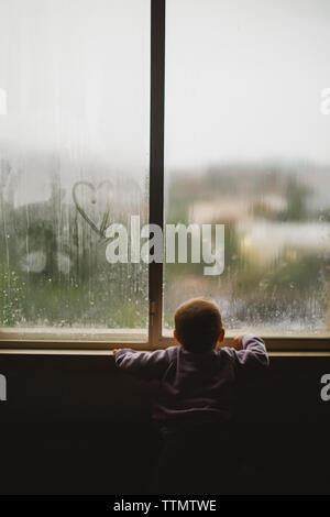 A baby girl looking through a window covered with steam and heart Stock Photo