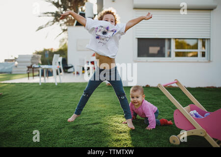 Two sisters  playing in the yard jumping near a baby stroller Stock Photo