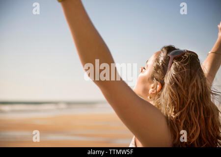 Side view of carefree woman raising arms at beach Stock Photo