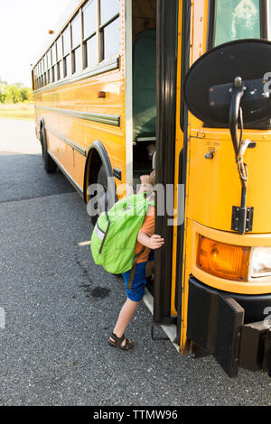 Boy getting in school bus on street Stock Photo