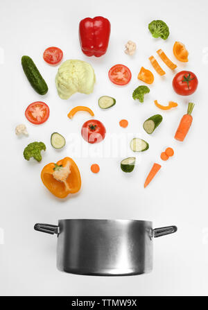 Fresh vegetables falling into a casserole pot on white background Stock Photo