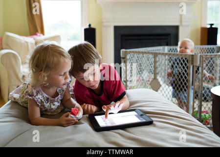 Baby boy looking at siblings using tablet computer while standing in crib Stock Photo