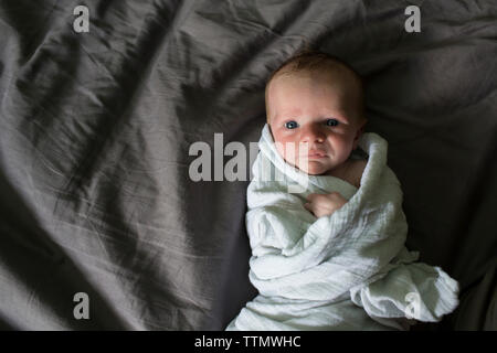 Overhead portrait of baby boy lying on bed while being wrapped in blanket Stock Photo