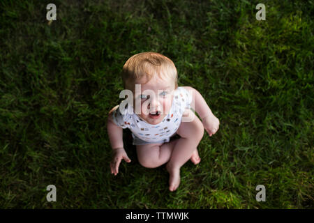 High angle portrait of cute baby boy sitting on grassy field at park Stock Photo