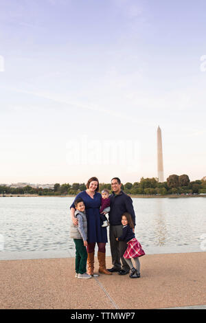 Portrait of smiling parents with children standing on footpath by lake against sky during sunset Stock Photo