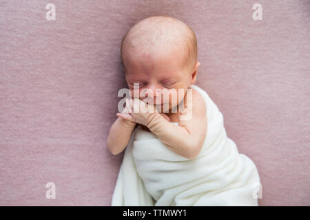 Newborn Baby Girl in White Wrap Laying on Pink Blanket, Sucking Thumb Stock Photo