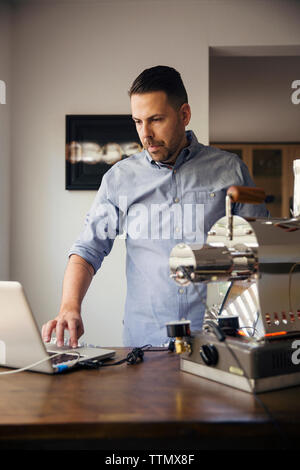 Man using laptop and coffee roaster in cafe Stock Photo
