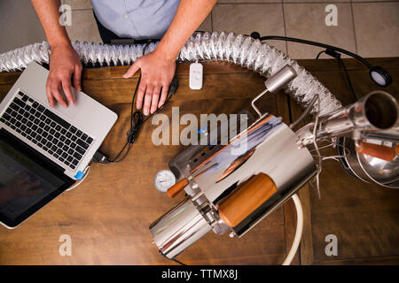 Overhead view of owner using laptop and coffee roaster at table Stock Photo