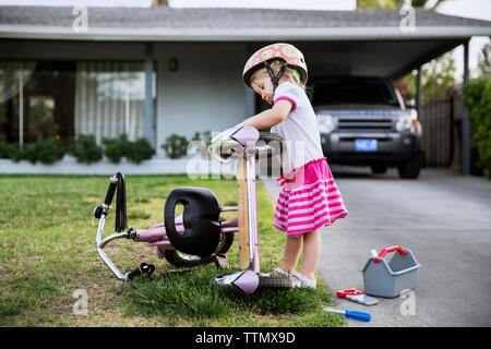 Side view of girl repairing bicycle on footpath outside house Stock Photo