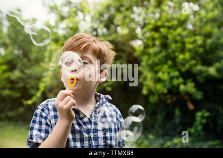 Thoughtful boy blowing bubbles in yard Stock Photo