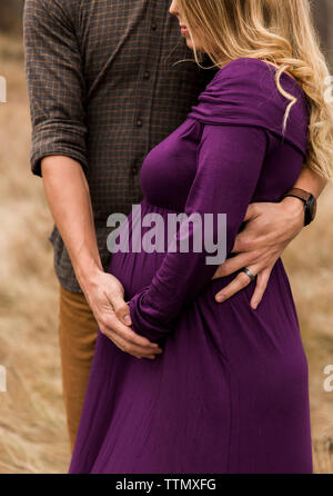 Midsection of husband embracing pregnant wife while standing outdoors Stock Photo