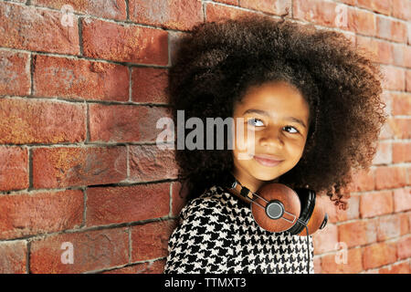 Afro-American little girl with headphones on brick wall background Stock Photo