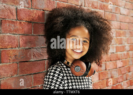 Afro-American little girl with headphones on brick wall background Stock Photo