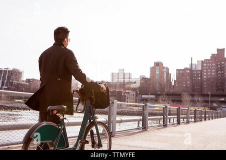 Rear view of businessman walking with bicycle on footpath in city Stock Photo