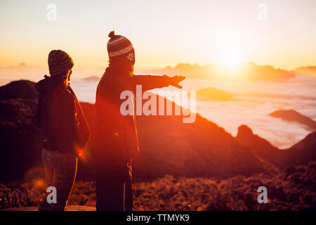 Man pointing while standing with woman on mountain during sunset Stock Photo