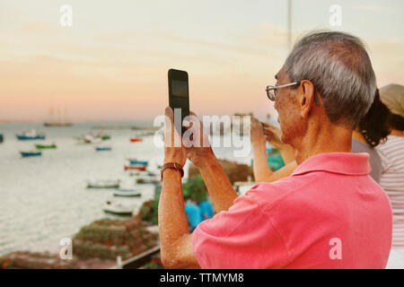 Senior man photographing through smart phone while standing with siblings at harbor Stock Photo