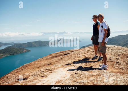 Friends looking at view while standing on mountain against sky during sunny day Stock Photo