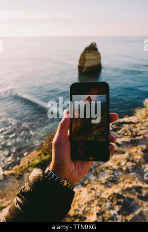 Cropped hand of man photographing sea with smart phone during sunset Stock Photo