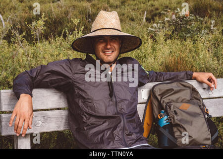 Portrait of smiling hiker with backpack wearing straw hat while sitting on bench at Wilsons Promontory National Park Stock Photo