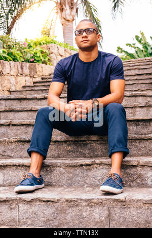 Thoughtful young man with hands clasped sitting on steps Stock Photo