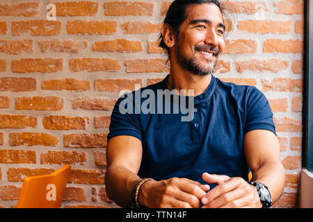 Smiling mature man looking away in cafe against brick wall Stock Photo