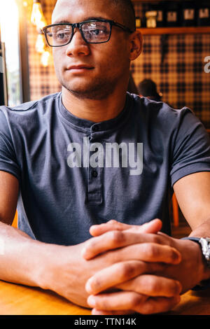 Thoughtful young man with hands clasped looking away in cafe Stock Photo