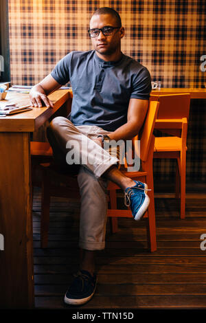 Full length of confident young man sitting on chair at cafe Stock Photo