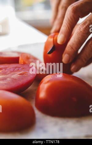 Cropped hands of woman cutting tomatoes on table in kitchen Stock Photo