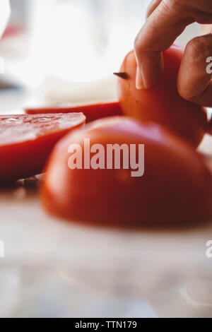 Cropped hands of woman cutting tomatoes on table in kitchen at home Stock Photo