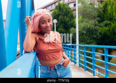 Portrait of smiling woman with pink hair standing by railing on footbridge Stock Photo