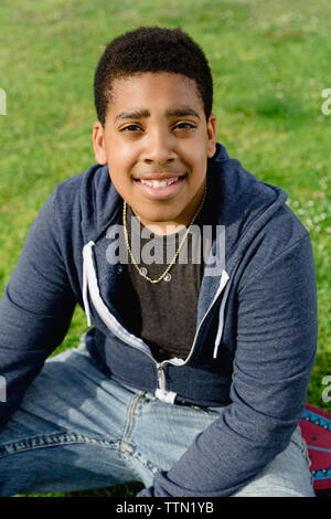 Portrait of smiling teenage boy sitting on field at park Stock Photo