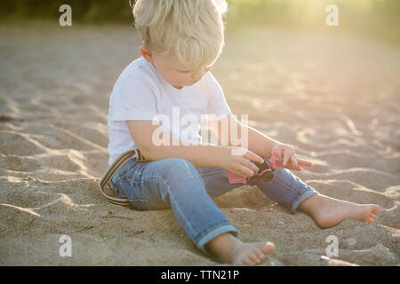 Baby boy playing with toy while sitting on sand at beach Stock Photo