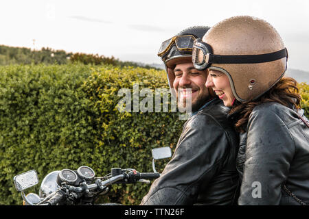 Cheerful couple talking while sitting on motorcycle against sky Stock Photo