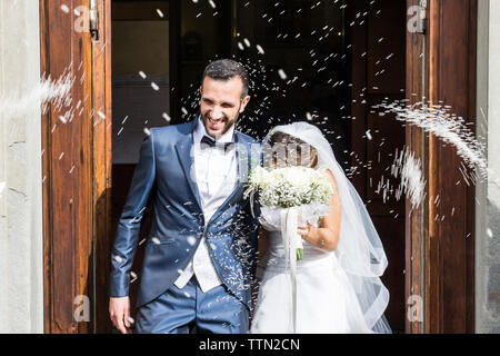 Confetti throwing on happy newlywed couple standing at church entrance Stock Photo