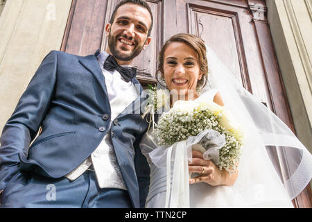 Low angle portrait of happy newlywed couple standing at church entrance Stock Photo
