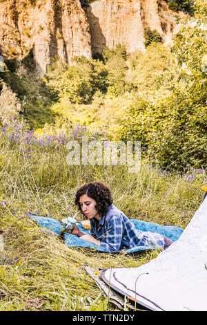 Woman having drink while relaxing on blanket at campsite in forest Stock Photo