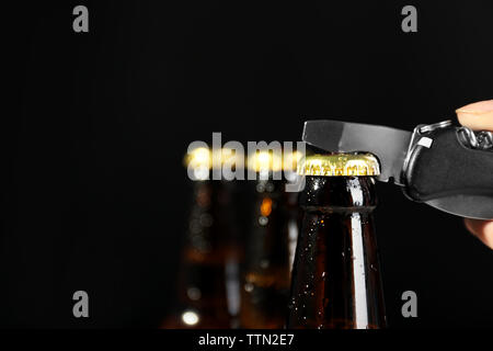 Female hand opening beer bottle on dark background Stock Photo