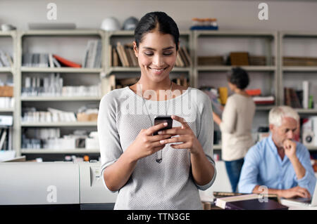 Happy interior designer using smart phone with colleagues working in background Stock Photo