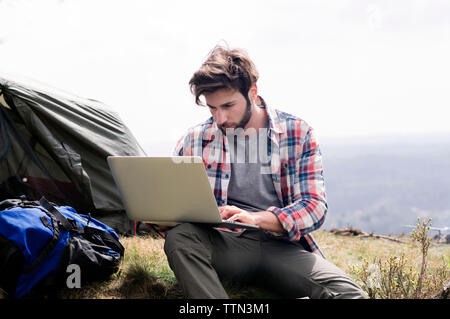 Man using laptop at campsite on hill against clear sky Stock Photo