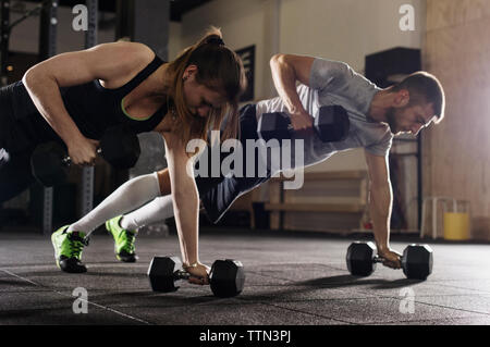 Determined male and female athletes doing push-ups while exercising with dumbbells in gym Stock Photo