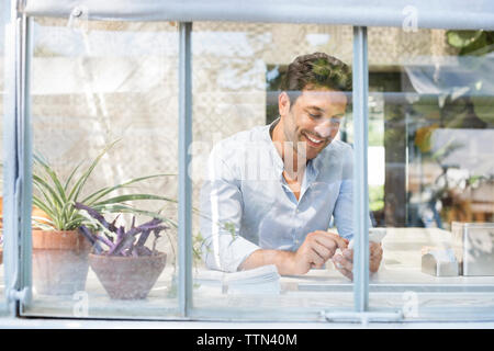 Happy man using smart phone at sidewalk cafe seen through glass window Stock Photo