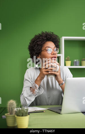 Thoughtful woman with laptop computer having coffee at office Stock Photo