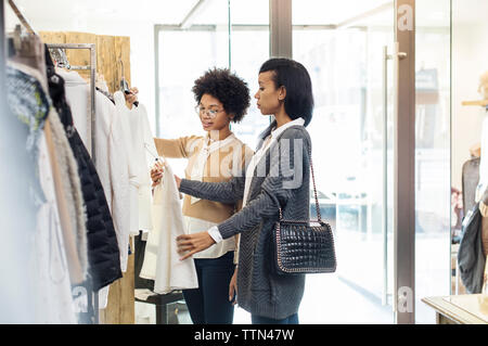 Friends talking while choosing shirts on clothes rack at store on sunny day Stock Photo